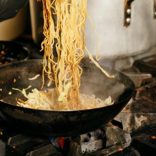 Noodles tossed in a wok over the flame